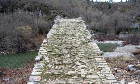 Photo for Greece Kalogeriko or Plakidas ancient stone bridge over Voidomatis river water, Zagoria Epirus. View from footbridge rocky path of winter dry tree. - Royalty Free Image