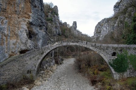 Photo for Greece Kokkorou Noutsou arched stone bridge over Voidomatis dry river Zagorohoria Epirus. Rocky landscape winter day dry tree background. - Royalty Free Image