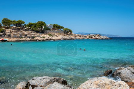 Téléchargez les photos : Grèce Plage d'Aponisos, destination Île d'Agistri. Plage rocheuse avec pins et parasol, baignade dans l'eau de mer turquoise, ciel bleu, journée ensoleillée. - en image libre de droit