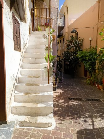 Crete island, Chania Old Town, destination Greece. Stonewall, stone stair, potted plant on narrow paved walkway. Summer sunny day. Vertical