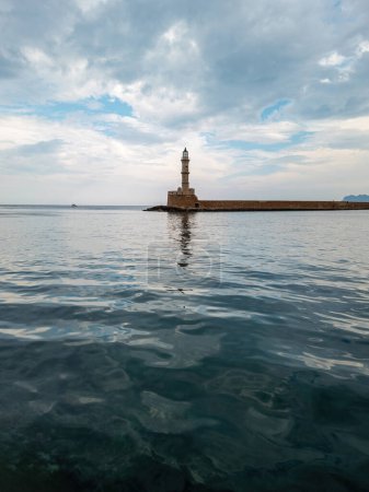 Beacon at Venetian harbour in Old Town of Chania. Reflection of lighthouse tower in wavy sea, stone breakwater. Crete island, Greece. Vertical