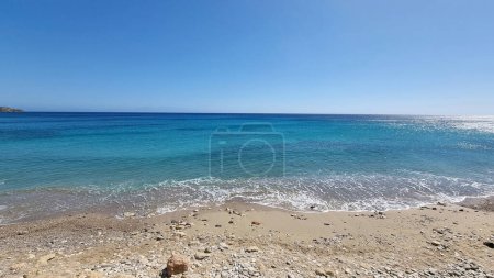Gavdos island, Sarakiniko nudist sandy beach, Crete Greece. White foam wets seaside sand. Wavy sea, sunny day, summer vacation, blue sky background.