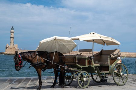 Chania Old Town, Crete, Greece. White horse drawn carriage and lighthouse at Venetian harbour,