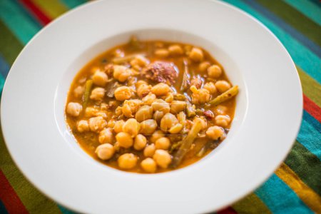 A bowl of traditional Andalusian chickpea and tagarninas stew served on a vibrant textile.