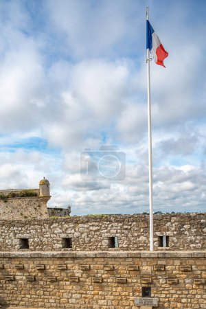 The French flag waving at Port Louis Citadelle in Lorient, Brittany, France. A historical fort with a scenic view and cloudy sky.