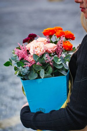 A woman holds a blue vase filled with flowers, providing a striking visual against a plain backdrop with ample copy space.