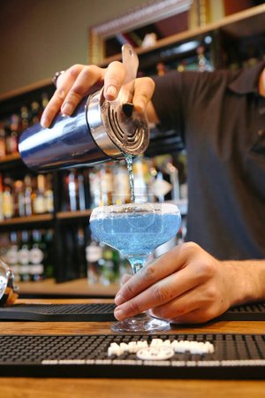 A bartender skillfully pours a delicious cocktail into a glass at a busy bar.