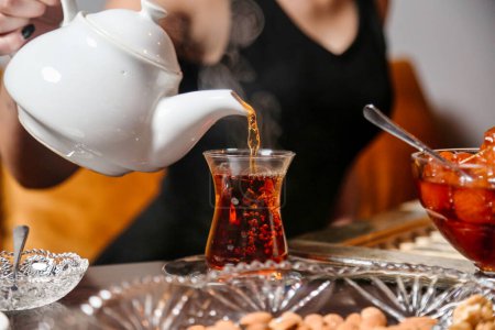 Eine Frau gießt vorsichtig Tee aus einem Wasserkocher in eine gläserne Teekanne.