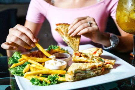 Una mujer come alegremente un sándwich y fríe en una mesa en un restaurante.