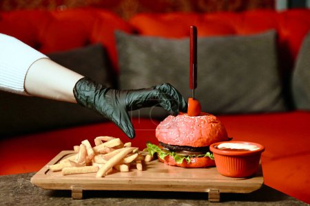 A person wearing black gloves carefully squeezing ketchup onto a hamburger.