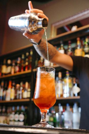 Ein Barkeeper im schwarzen Hemd gießt einen dosierten Schuss Whiskey in ein schräg gehaltenes Martini-Glas.