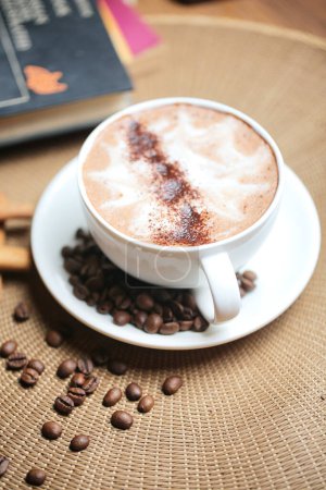 Un cappuccino est placé sur une soucoupe et entouré de grains de café pour une expérience riche et aromatique.