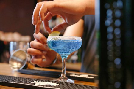 Une personne place soigneusement une tranche de citron frais dans un verre à cocktail rempli d'une boisson rafraîchissante.