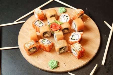 Téléchargez les photos : Une assiette en bois garnie d'une variété de rouleaux de sushi et accompagnée d'une paire de baguettes pour manger. - en image libre de droit
