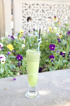 A glass of vibrant green drink placed on a sturdy cement table outdoors.