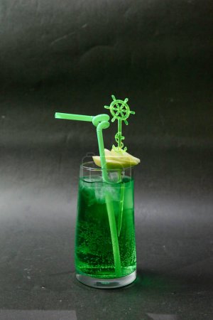 A clear glass containing a vivid green drink with a slender green straw placed in it.