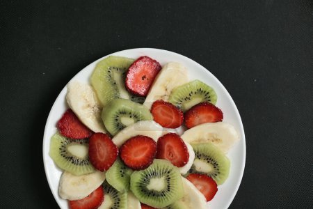 A white plate adorned with freshly sliced kiwi fruit and strawberries arranged neatly.