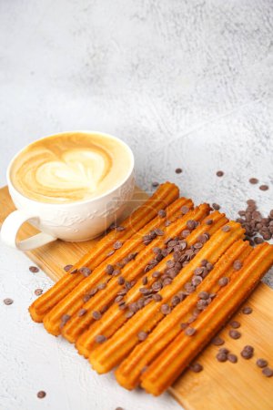 A wooden cutting board is shown with chocolate chips placed neatly on top, accompanied by a cup of steaming hot coffee.