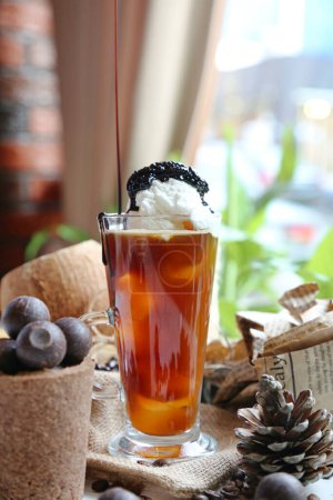 Téléchargez les photos : Un grand verre rempli de thé glacé et surmonté d'une cuillerée de crème fouettée. - en image libre de droit