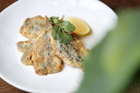 Un plato blanco exhibe un pescado deliciosamente cocinado cubierto con una rebanada de limón.