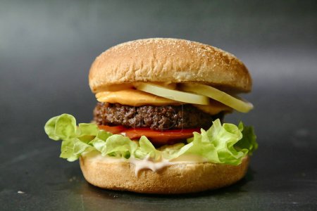 Téléchargez les photos : Un délicieux hamburger garni de laitue fraîche et de tranches de tomate juteuses, placé sur une surface noire élégante et moderne. - en image libre de droit