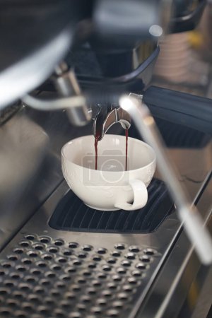 Eine Hand gießt eine Tasse Kaffee in die Kaffeemaschine.