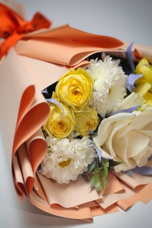Ein atemberaubender Strauß weißer und gelber Blumen, fein säuberlich in orangefarbenes Papier gewickelt, mit viel Kopierraum.