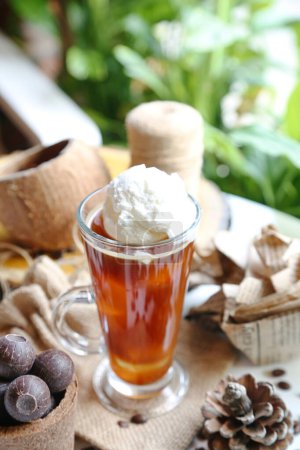 A cup of tea featuring whipped cream on top and a tea bag steeping in the hot water.