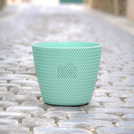 A green cup sits on a cobblestone road, providing a simple yet serene scene.