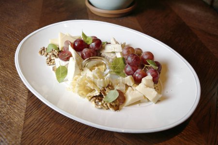 Photo for A white plate is elegantly adorned with fresh grapes and a variety of delectable cheeses. - Royalty Free Image
