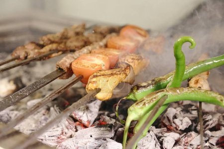 A detailed view of various food items being cooked on a grill, with the flames and smoke adding to the cooking process.