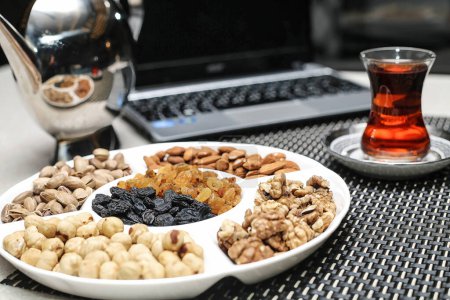 A plate containing a variety of nuts placed next to a cup of hot tea on a wooden table.