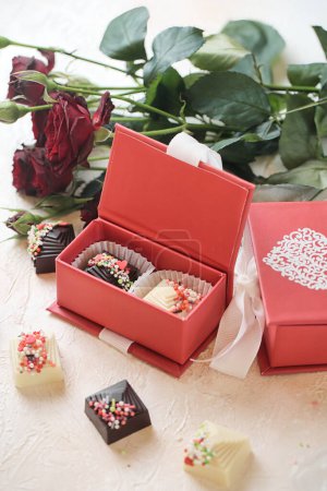 Téléchargez les photos : Une boîte rouge remplie de chocolats est placée à côté d'un magnifique bouquet de roses. - en image libre de droit