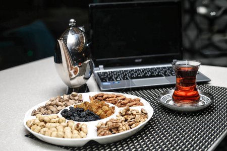 Téléchargez les photos : Une assiette remplie de diverses noix placées à côté d'une tasse de thé fumant. - en image libre de droit
