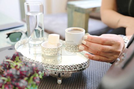 Una mujer es vista sosteniendo una taza de café firmemente sobre una mesa.