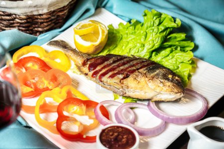 Photo for A white plate showcases a deliciously cooked piece of fish, topped with a colorful array of fresh vegetables. - Royalty Free Image