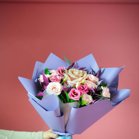 A person gracefully holds a vibrant bouquet of flowers against a soft pink background, creating a visually appealing composition with plenty of copy space.