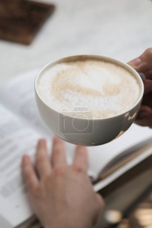 Téléchargez les photos : Une personne tient doucement une tasse de café sur un livre ouvert. - en image libre de droit