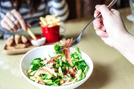 A person is seen eating a salad with a fork.