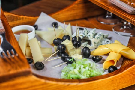 Photo for A wooden tray is filled with an assortment of cheese and olives, creating a delectable display of flavors and textures. - Royalty Free Image