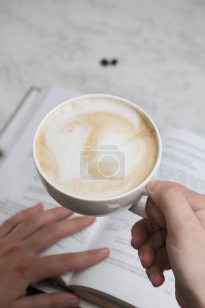 Una persona sostiene una taza de café humeante en un café bullicioso
