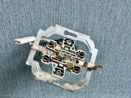 Un interruptor de luz roto se encuentra en una alfombra azul, con daños visibles y cables expuestos.