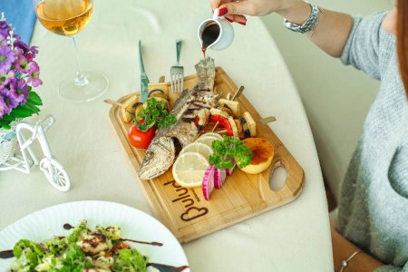 Téléchargez les photos : Une femme est assise à une table, dégustant un repas avec une assiette de nourriture devant elle. - en image libre de droit