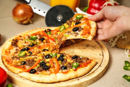 Une personne est vue prendre une tranche de pizza d'une tarte chaude et fraîchement cuite dans une pizzeria locale.