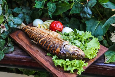 Téléchargez les photos : Un poisson frais repose sur une planche à découper en bois, entouré de laitue vibrante et de tomates mûres. - en image libre de droit