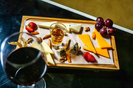 Photo for A glass of red wine accompanied by a selection of different cheeses arranged neatly on a wooden tray. - Royalty Free Image