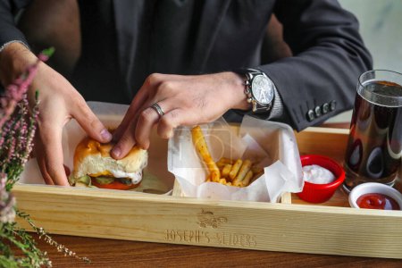 A man dressed in a suit is seen enjoying a sandwich and french fries.