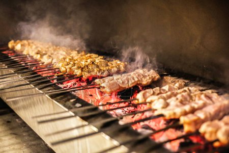 A variety of food items, including meats, vegetables, and seafood, sizzle and cook on a grill.