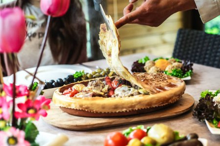 Foto de Una persona hábilmente corta una pizza encima de una mesa, usando un cuchillo afilado. - Imagen libre de derechos