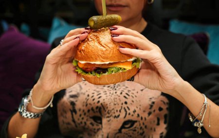 A woman holding a large hamburger in front of her face, displaying her enjoyment of the food.